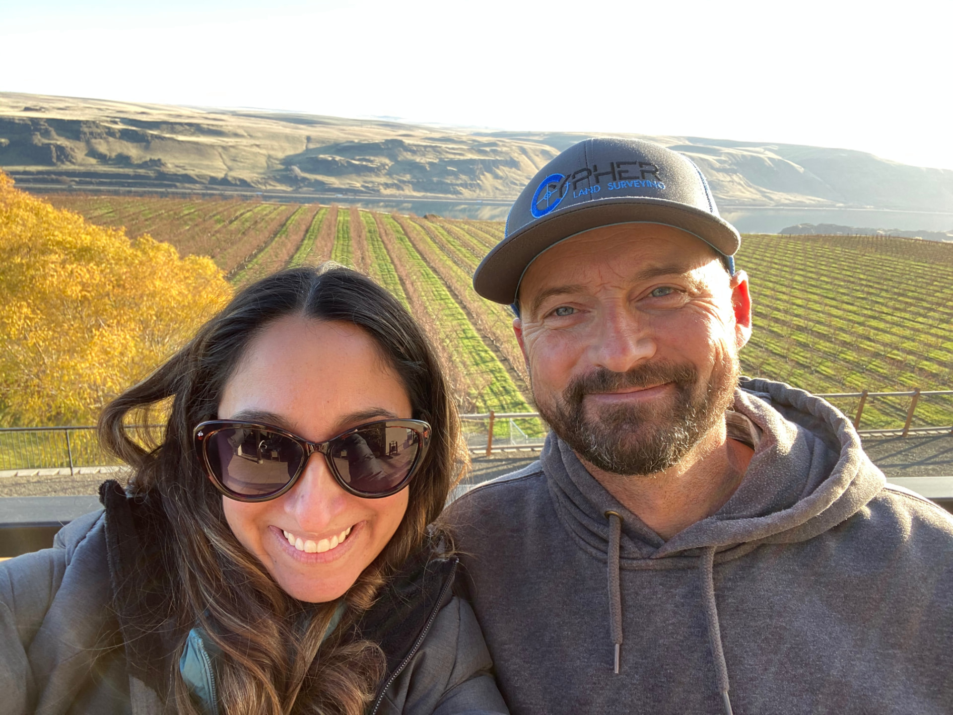 Melissa and Jerad Robbins smiling together in front of a vineyard on a sunny autumn day